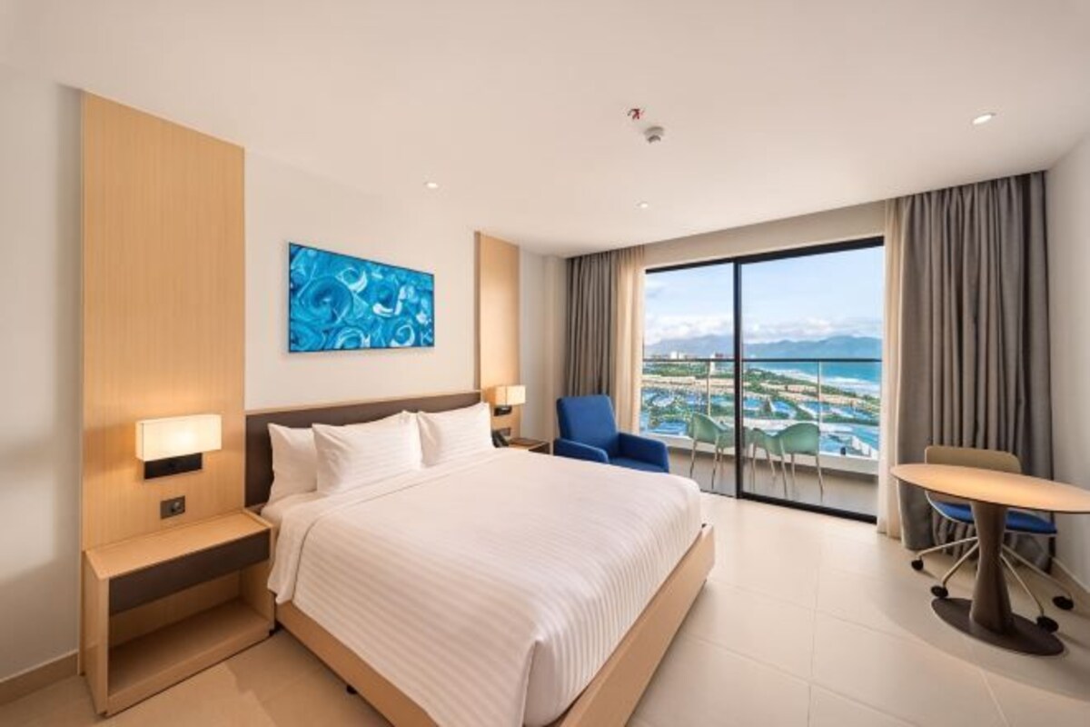 A hotel room with a large bed, a desk, a chair, and a view of the ocean.