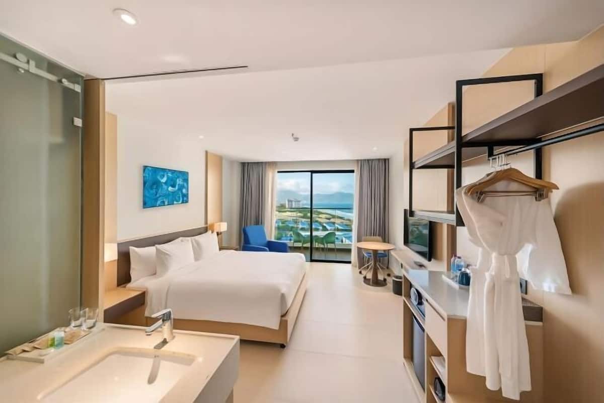 A hotel room with a bed, a desk, a TV, a window with a view, and a robe hanging on a rack.