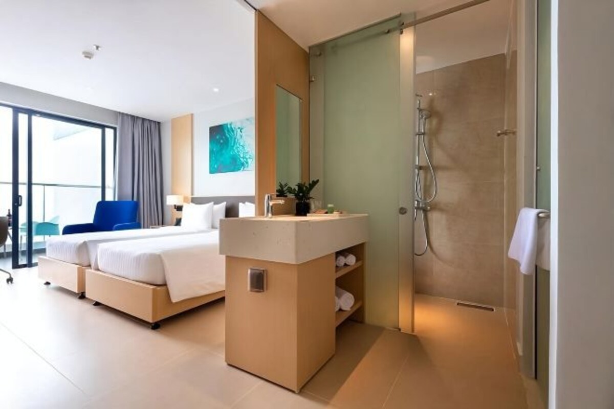 Habitación de hotel moderna con cama, mesita de noche, zona de ducha y un amplio ventanal.
