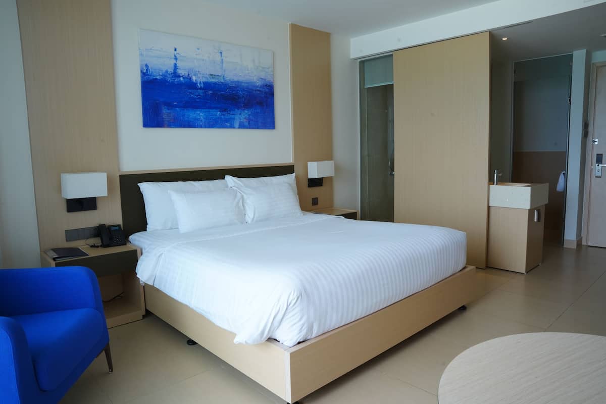 A modern hotel room with a large bed, bedside tables, a desk, a chair, and a painting on the wall.