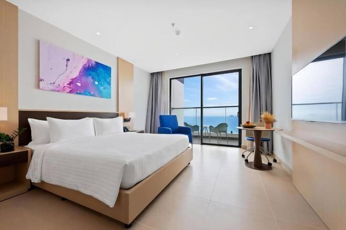 A modern hotel room with a large bed, a desk, a chair, and a balcony with a view.