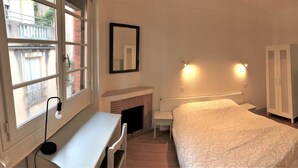 A bedroom with a bed, a desk, a chair, a fireplace, a wardrobe, and a window with a view of a balcony. - Family apartment near Lot (CAHORS)