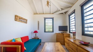 Una habitación acogedora con un banco de madera, un sofá colorido, un televisor y una ventana con persianas.
