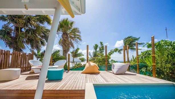 Una terraza de madera con piscina, sillas de descanso y vistas a palmeras.
