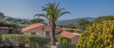 A Mediterranean-style villa with a red-tiled roof, surrounded by lush greenery and a clear blue sky.