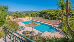 A pool with lounge chairs, surrounded by greenery and a view of hills.