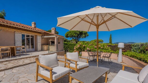 An outdoor patio with stone flooring, wooden furniture, and a large umbrella.