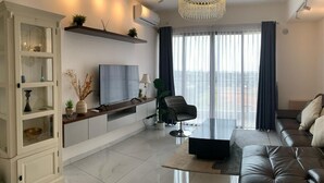 A modern living room with a glass coffee table, a leather sofa, a white cabinet, and a large window with curtains. - Morich suites BSD (Pagedangan)