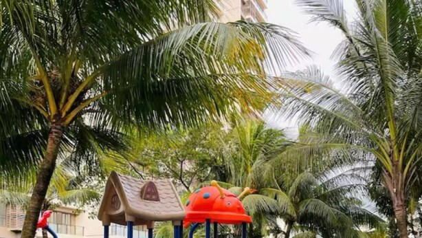 A children's playground with slides and climbing structures, surrounded by palm trees and a water feature. - Morich suites BSD (Pagedangan)