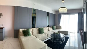 A modern living room with a sectional sofa, a glass coffee table, and a large window with curtains. - Morich suites BSD (Pagedangan)