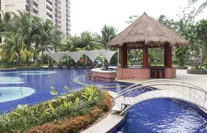 A swimming pool with a thatched-roof gazebo, surrounded by palm trees and lounge chairs. - Morich suites BSD (Pagedangan)