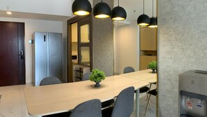 A modern dining area with a long table, grey chairs, and black pendant lights. - Morich suites BSD (Pagedangan)