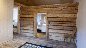 Ein rustikales Blockhaus-Interieur mit einem Bett, einem Sessel und einer Tür zu einem weiteren Raum.