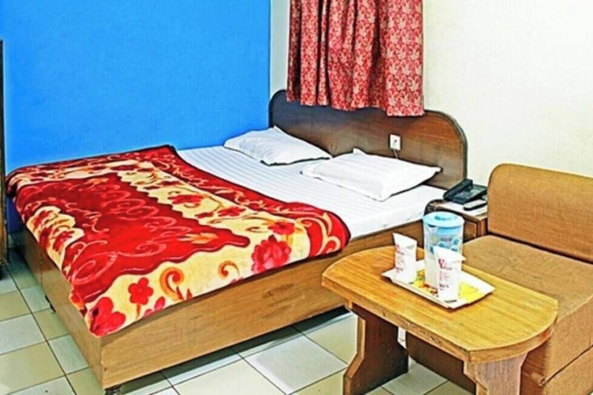 Een kamer met een bed, een houten nachtkastje, een stoel en een kleine tafel met een fles en een beker.