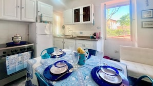 Una cocina compacta con gabinetes blancos, un refrigerador, una estufa y un comedor con una mesa preparada para dos.