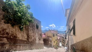 Una calle empedrada estrecha flanqueada por edificios, con una rejilla de metal en el suelo y un cielo azul despejado.