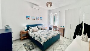 Un dormitorio con cama, mesitas de noche, un armario, una lámpara colgante y un ventanal con cortinas.