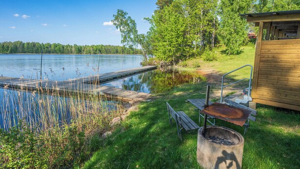 Una cabaña junto al lago con un muelle que se adentra en el agua, rodeada de vegetación y árboles.