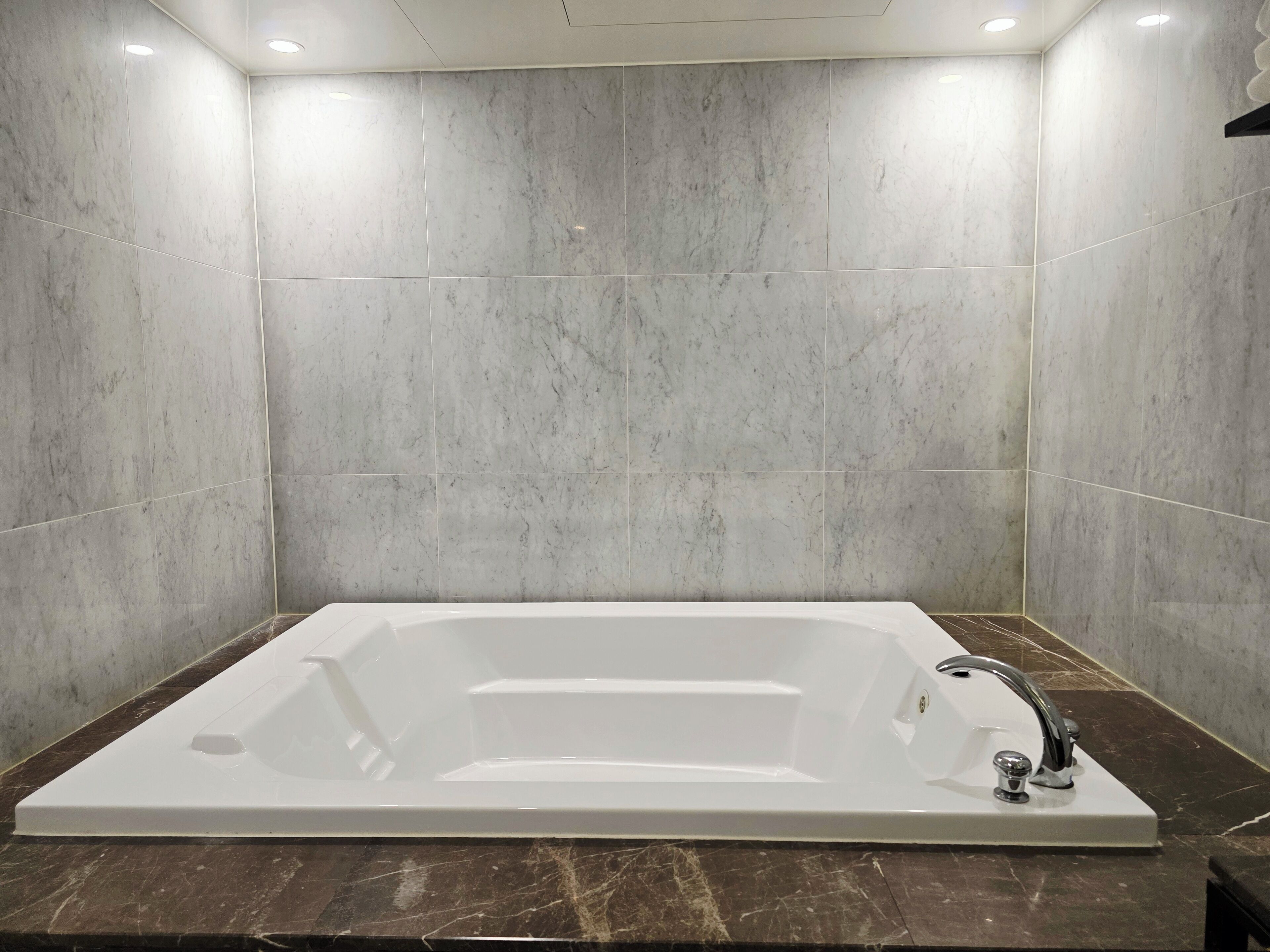 A modern bathroom with a large rectangular bathtub, marble walls, and a dark marble countertop.
