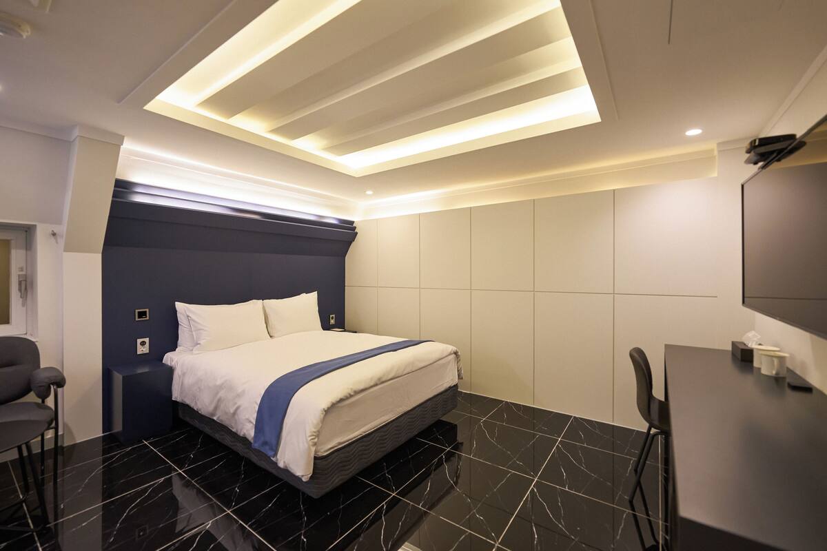 A modern hotel room with a large bed, a desk, and a chair.