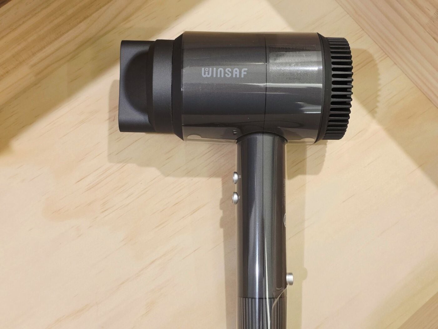 A black Winsaf hair dryer with a cylindrical shape and a ribbed nozzle, placed on a wooden surface.