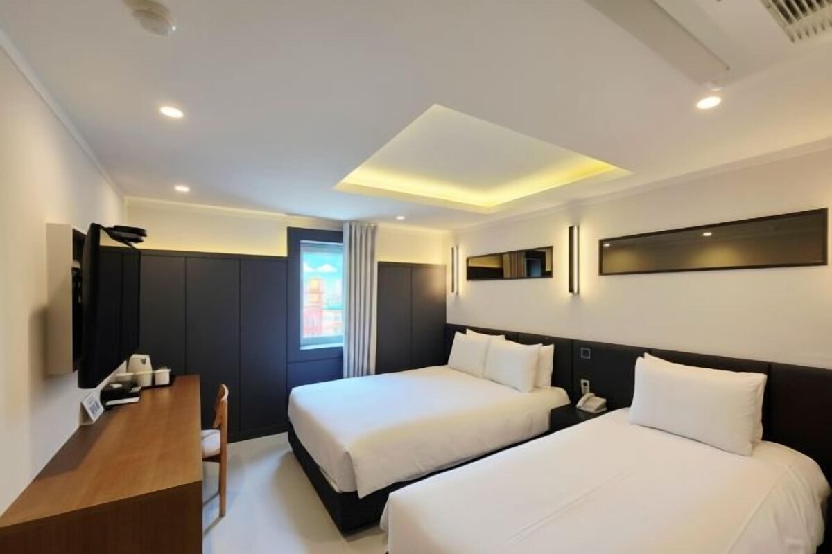 A hotel room with two beds, a desk, and a TV.