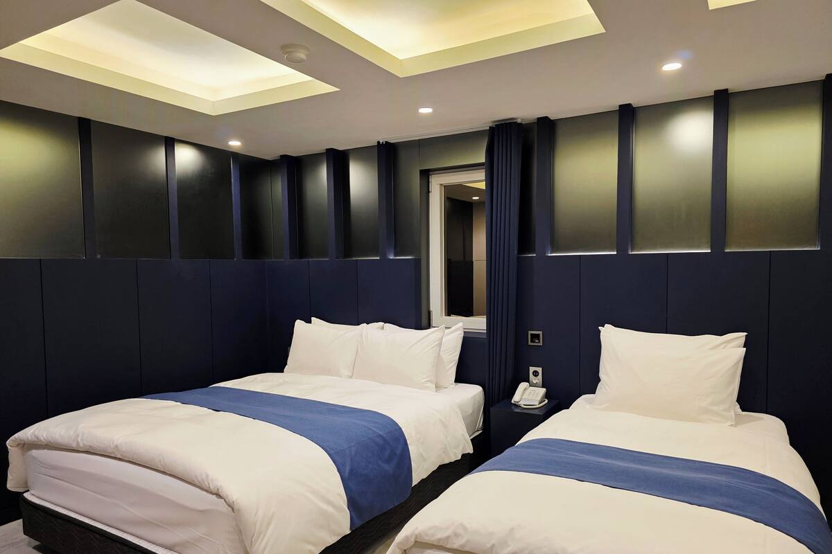 A hotel room with two beds, dark blue walls, and recessed ceiling lighting.