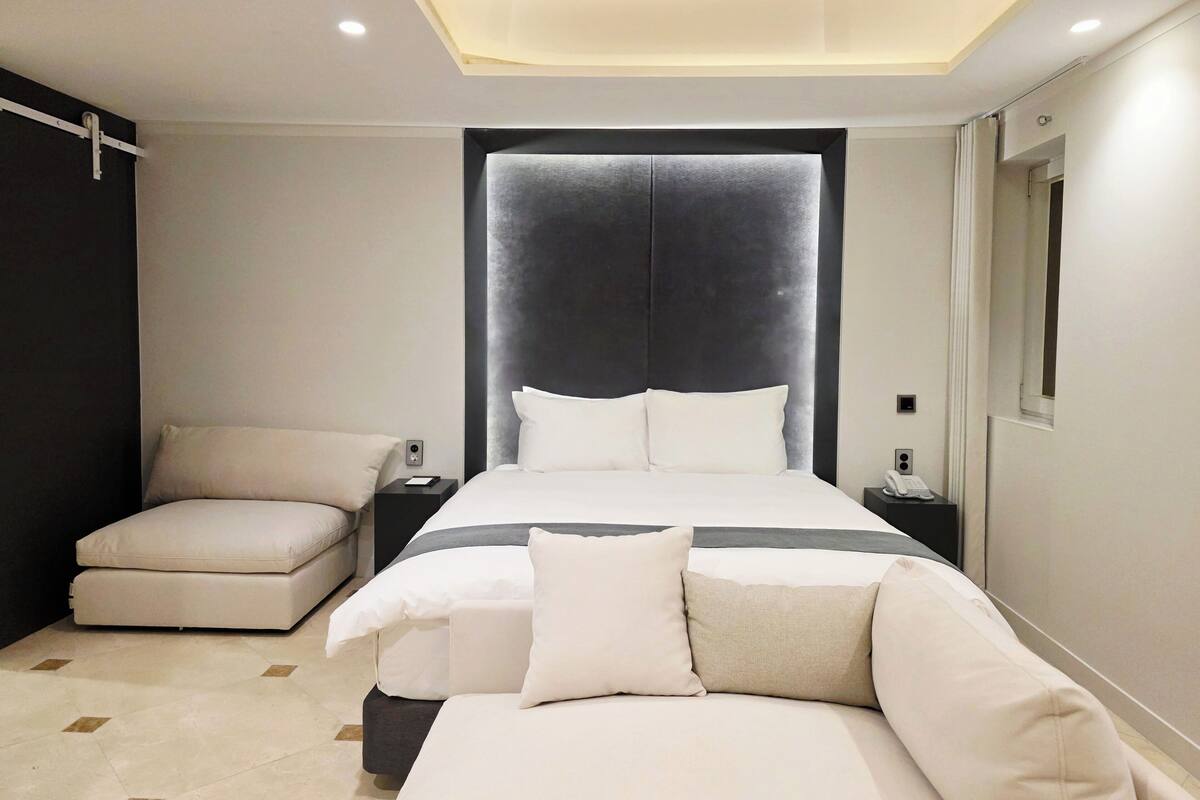 A modern bedroom with a large bed, bedside tables, a sofa, and a ceiling light fixture.