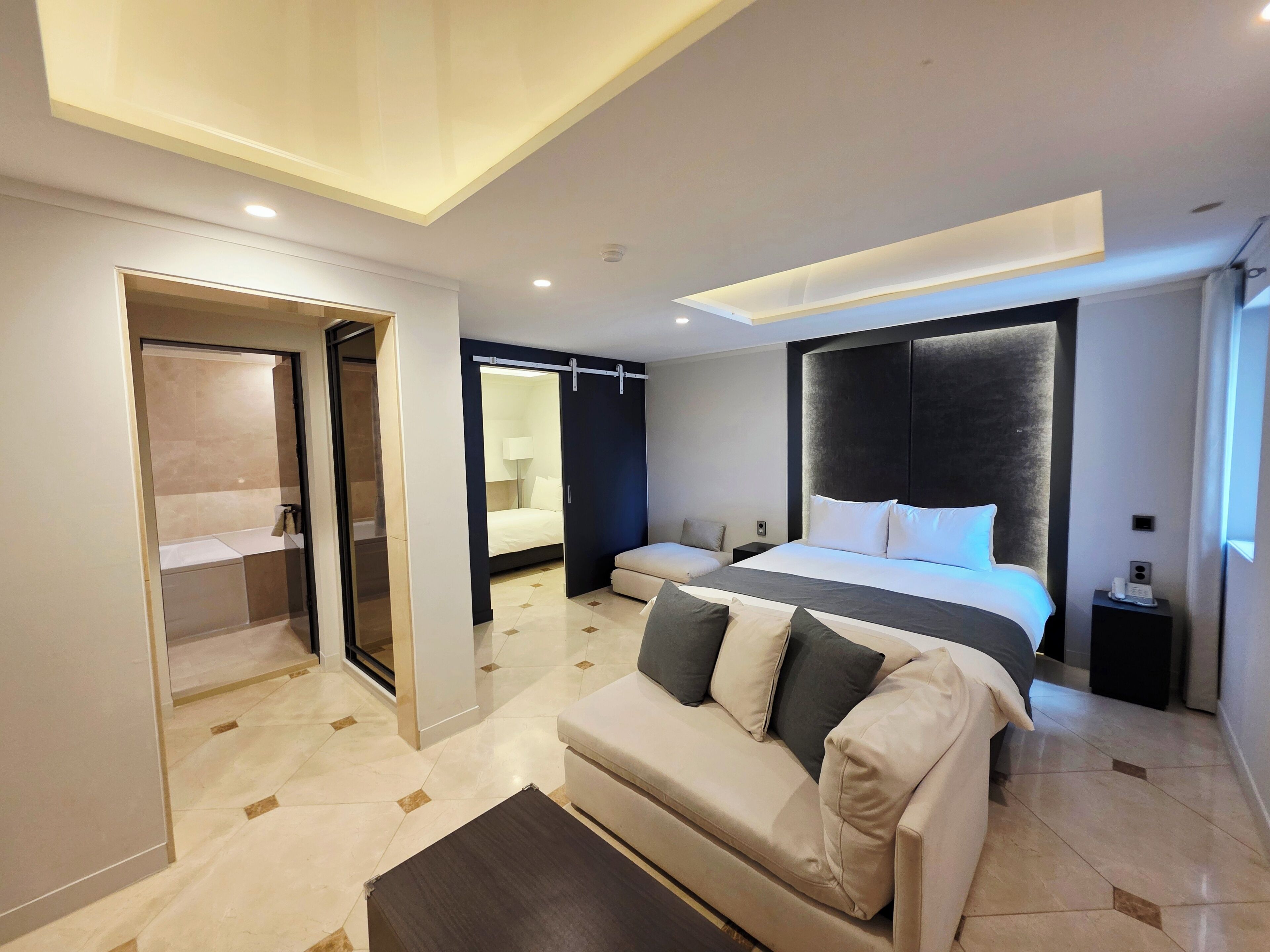 Una habitación de hotel moderna con una cama grande, un sofá, un vestidor y un baño con ducha e inodoro.