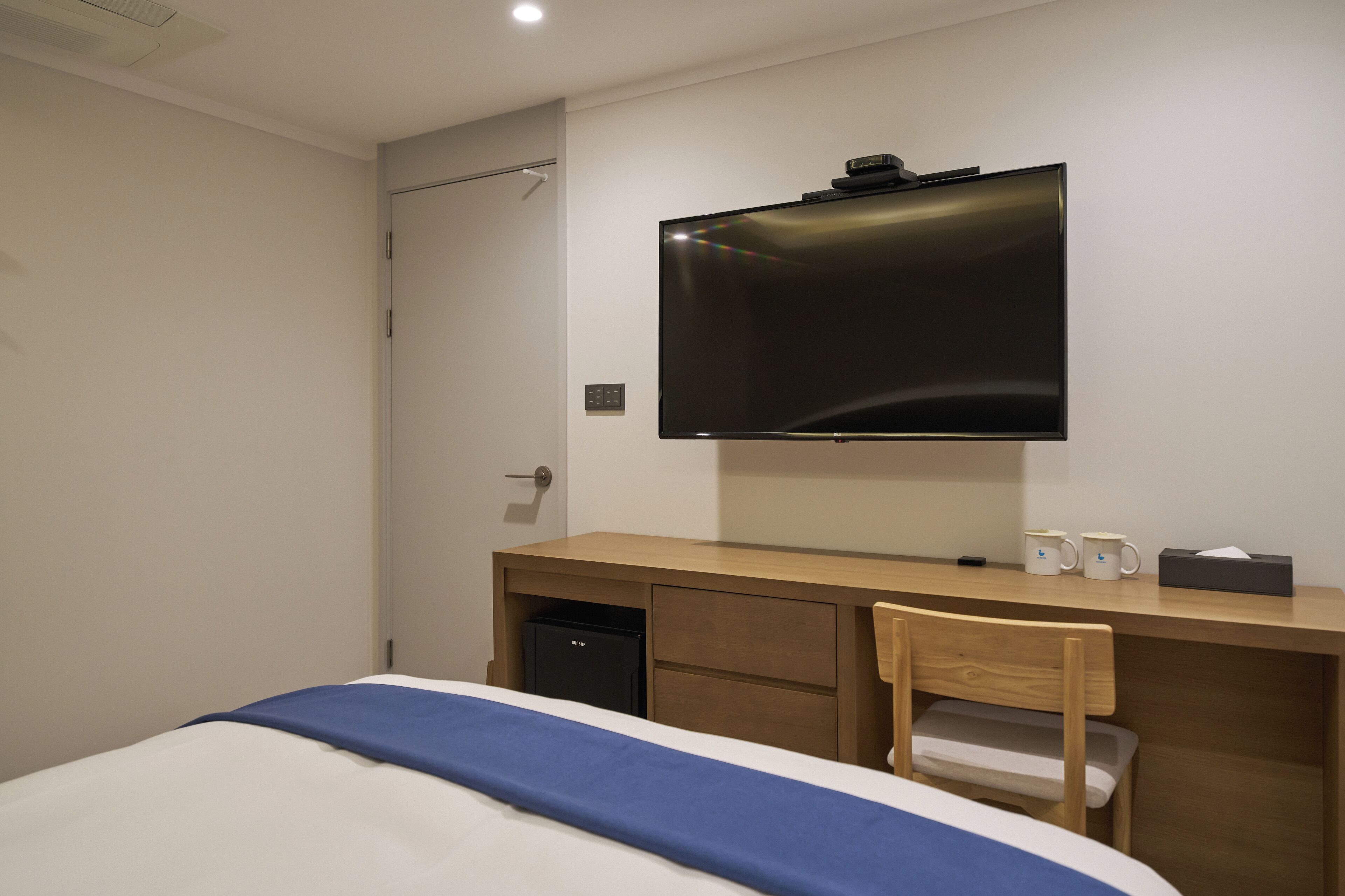 Une chambre d’hôtel comprenant un lit, un bureau avec une télévision, une chaise et un petit réfrigérateur.