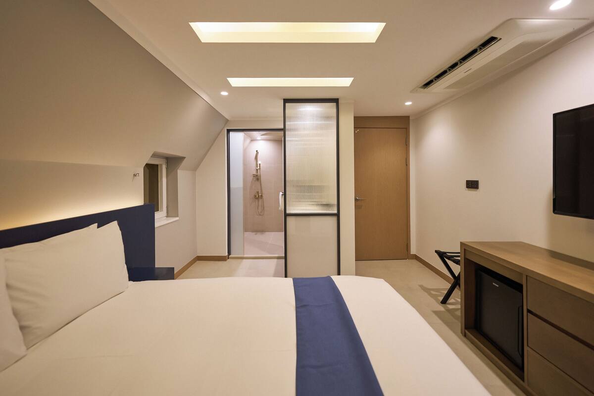 A modern hotel room with a large bed, a TV, a desk, and a walk-in closet.