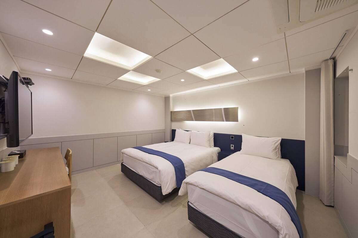 A hotel room with two beds, a desk, and a television.