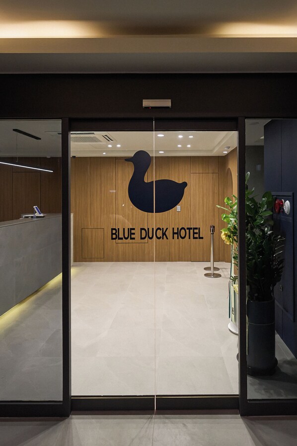 The entrance to the Blue Duck Hotel with a reception desk and a large logo on the wall. - BlueDuck Hotel (Seoul)