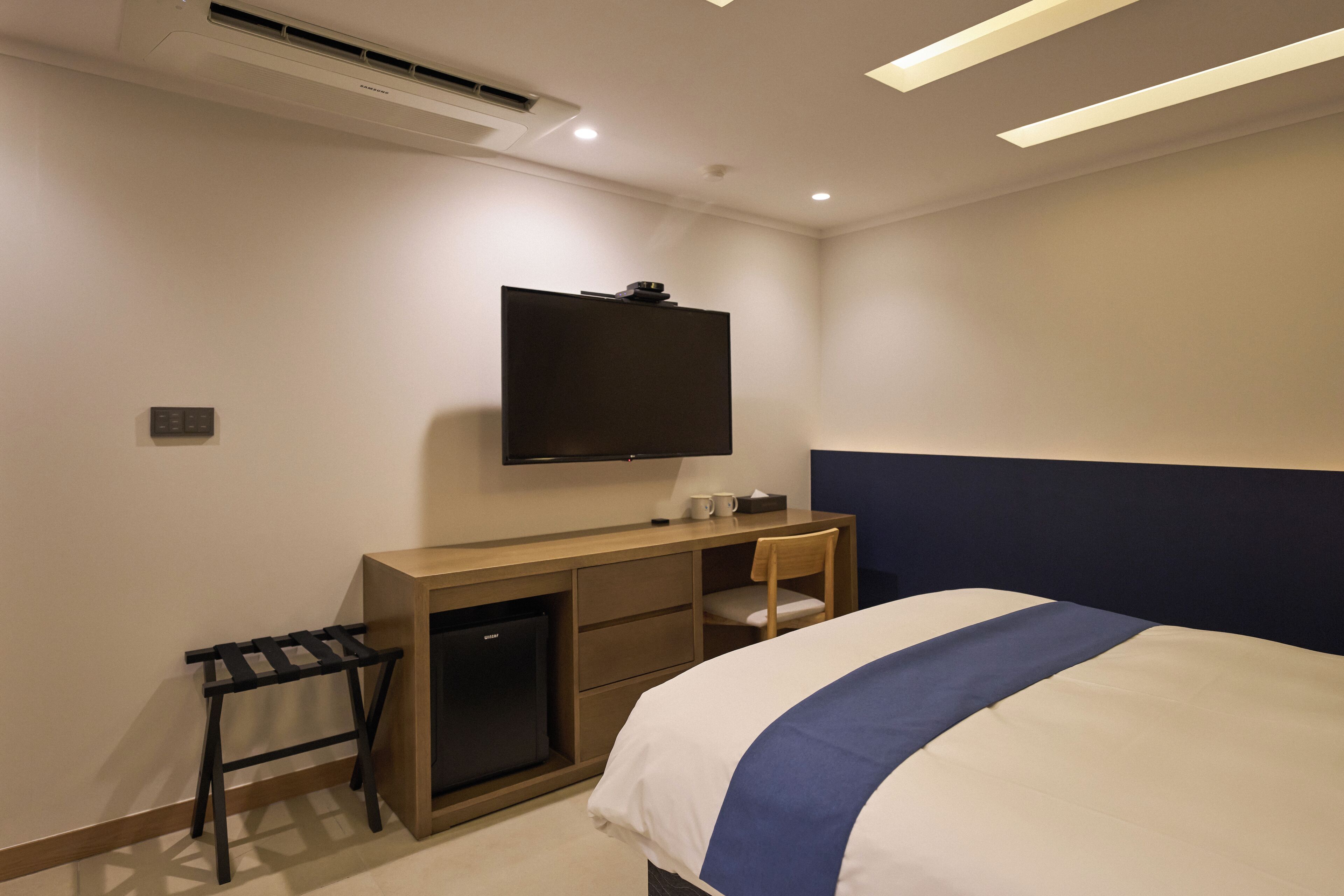 Una habitación de hotel con cama, escritorio, televisor y un refrigerador pequeño.