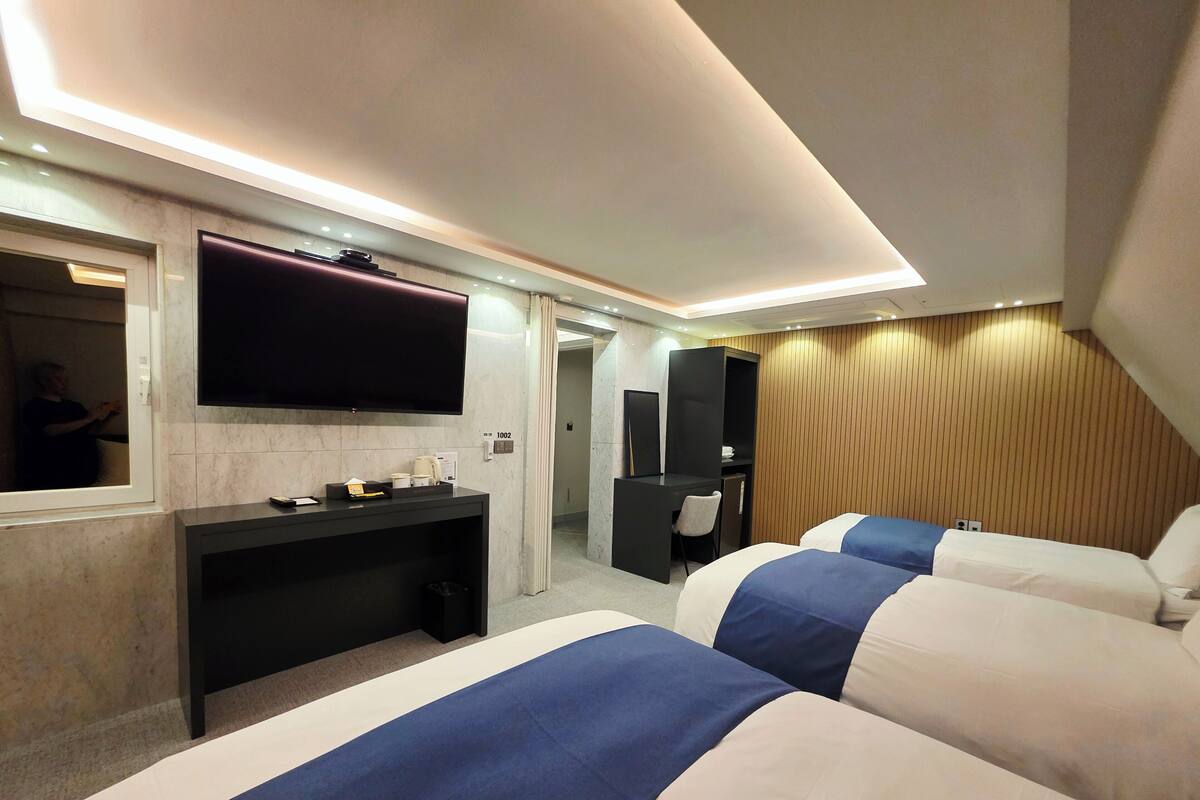 A hotel room with two beds, a desk, a TV, and a mirror.