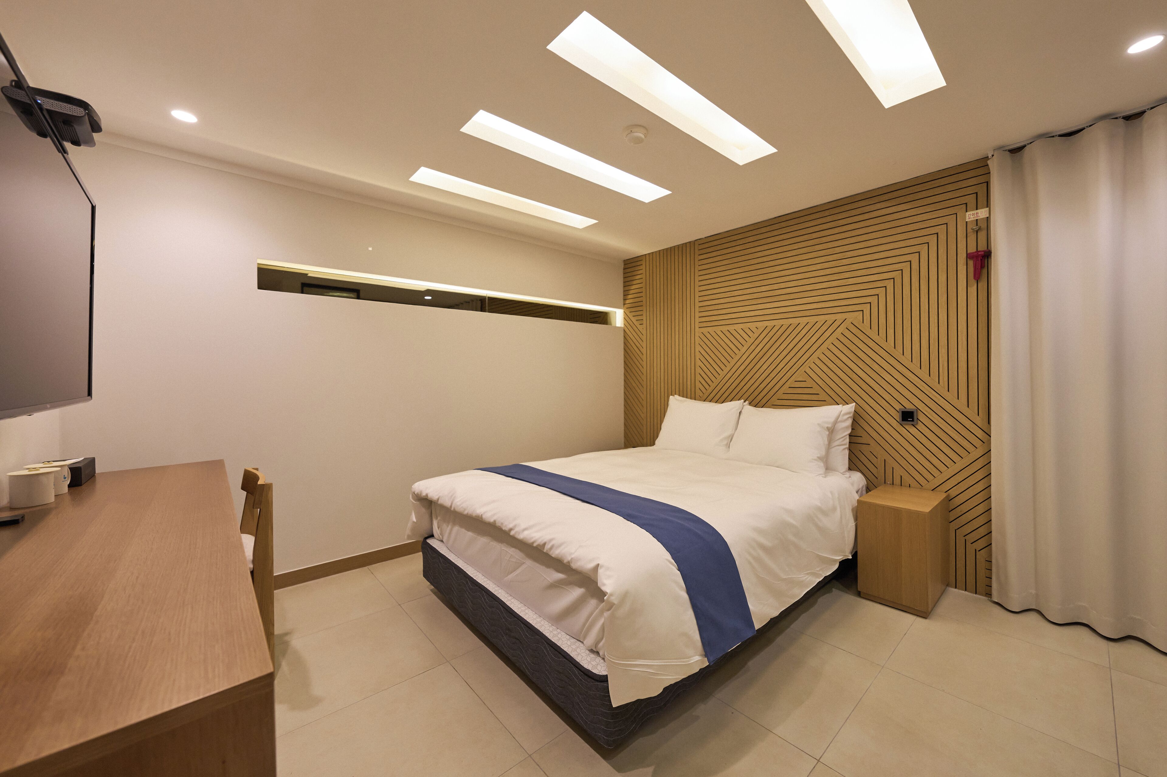 Una habitación de hotel moderna con una cama bien hecha, una mesita de noche de madera, un escritorio y un televisor.