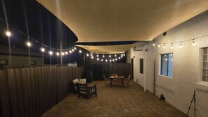 A covered patio area with a brick floor, a wooden table and chairs, and string lights.