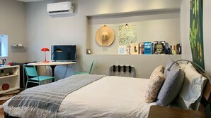 A bedroom with a bed, a desk, a chair, a TV, and a wall-mounted air conditioner.