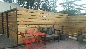 A patio area with a wooden fence, a bench, and two red chairs.