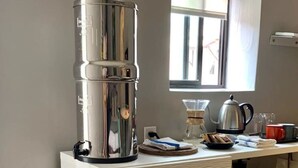 A kitchenette with a coffee maker, kettle, and various kitchen items on a white cabinet.