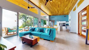 A spacious living area with a large teal sofa, wooden coffee table, and a view of the outdoors through large windows. - Private Villa Oro Verde, ocean view, luxury (Uvita)