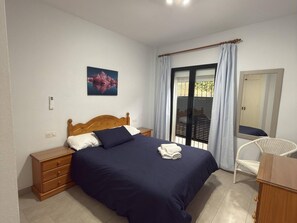 A bedroom with a wooden bed, a nightstand, a chair, a window with curtains, and a painting on the wall.