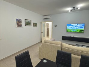 Un salon avec un canapé beige, une table basse noire et un téléviseur à écran plat fixé au mur.
