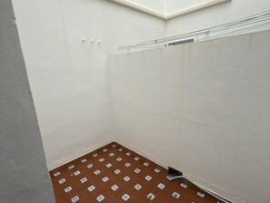 Un petit espace douche fermé, doté d’un sol carrelé et d’une étagère en métal pour suspendre des objets.