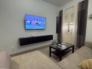 Un salon avec un téléviseur à écran plat fixé au mur, un meuble de rangement noir en dessous, une table basse avec un plateau en verre et un canapé beige.