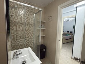 A bathroom with a glass-enclosed shower, a white sink, and beige tiled walls.