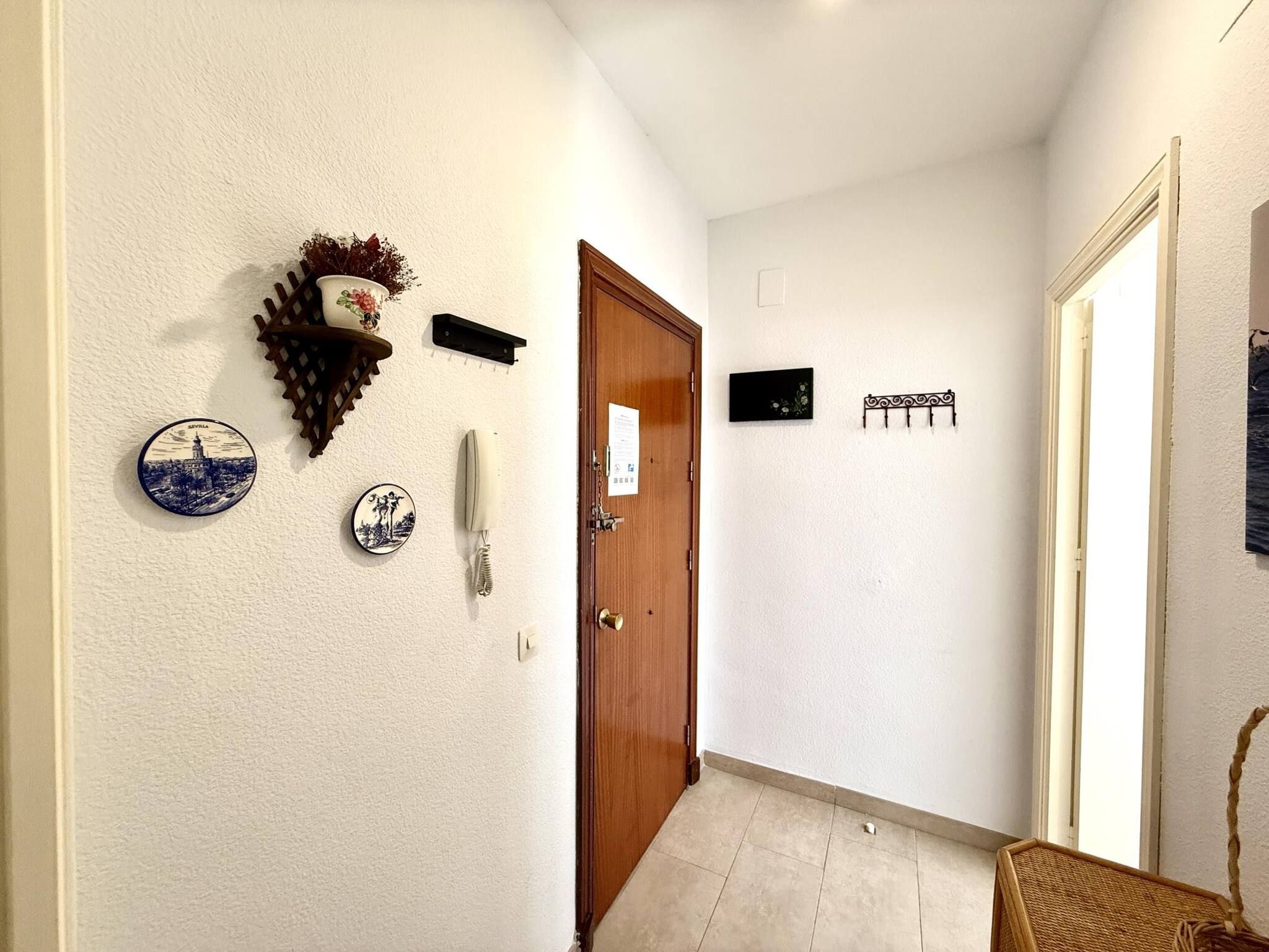 A hallway with a wooden door, a wall-mounted telephone, decorative plates, and a wall-mounted light fixture.