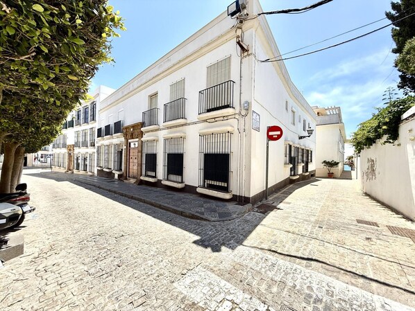 A narrow cobblestone street with a white building featuring multiple balconies and a red 'no entry' sign.