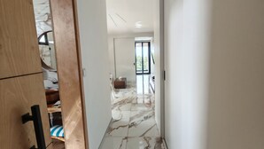 A hallway with a marble floor, a wooden door, and a view into another room with a window. - Modern Seaview Condo w/ Pool & Balcony – Steps to Beach (Cabarete)
