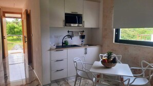 A modern kitchen with white cabinets, a microwave, and a dining area with white chairs and a table. - Modern Seaview Condo w/ Pool & Balcony – Steps to Beach (Cabarete)